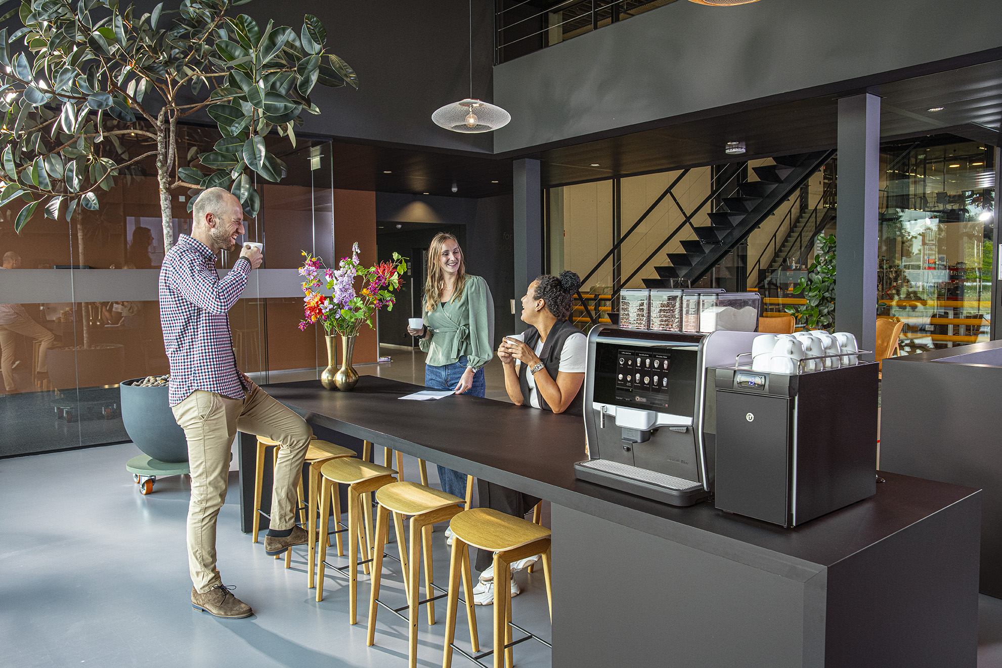 Kaffestation på moderne kontor med kolleger, der taler over en kop kaffe